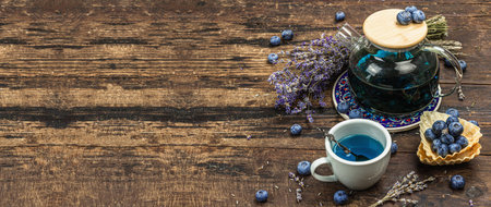 The concept of rustic style tea. Lavender flowers and blueberries. Vintage arrangement, hard light, dark shadow, wooden background, banner formatの写真素材