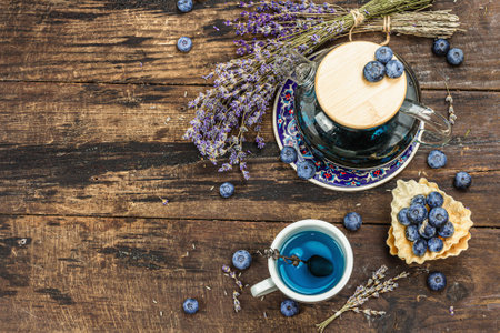 The concept of rustic style tea. Lavender flowers and blueberries. Vintage arrangement, hard light, dark shadow, wooden background, top viewの写真素材