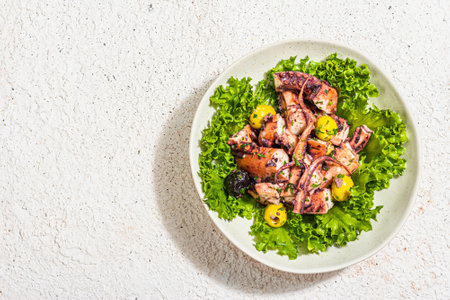 Octopus salad with lettuce, olives and spices in a bowl. Fresh and healthy seafood, marine decor. Trendy hard light, dark shadow, plaster background, top viewの写真素材