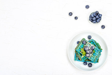 Homemade Belgium Waffles with blueberries. Gluten-free blue dessert, fresh fruits and mint. Trendy hard light, dark shadow. White plaster background, top viewの写真素材