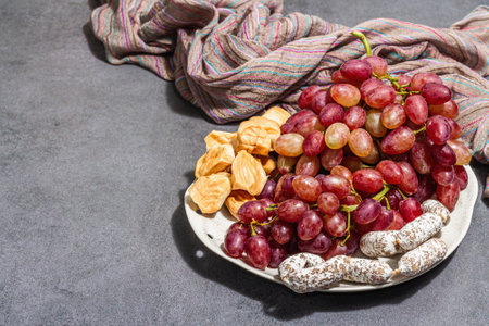 Snack plate with cheese, grapes and dried sausages. Charcuterie antipasto, stone concrete background. Trendy hard light, dark shadow, flat lay, copy spaceの写真素材