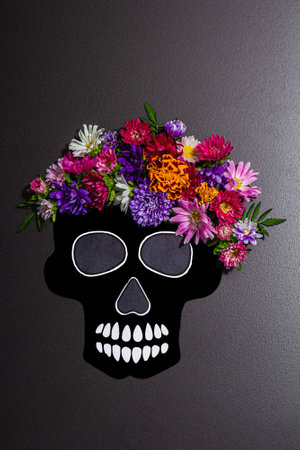 Paper human skull for Mexico's Day of the Dead (El Dia de Muertos) with traditional flowers. Trendy hard light, dark shadow. Black stone concrete background, top viewの写真素材
