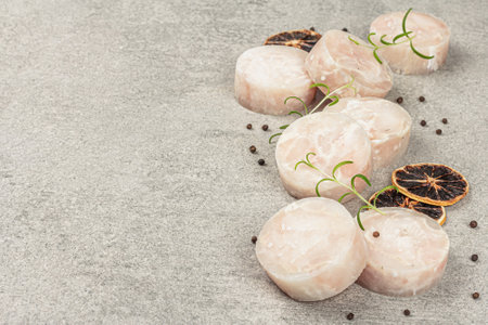 Chunks of frozen hake. Marine fish fillet on stone background, raw ingredient for cooking healthy food. Spices, fresh rosemary, lemon, copy spaceの写真素材