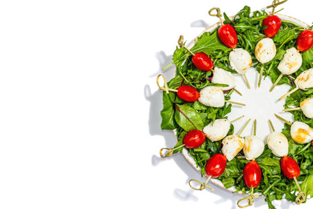Charcuterie wreath isolated on white background. Mozzarella, cherry tomatoes, and arugula on skewers. Fashionable snacks, festive vegetarian food, trendy hard light, dark shadow, top viewの写真素材
