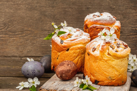 Easter cake Cruffin or sweet bread kulich with painted eggs. Traditional festive baking and fresh cherry flowers, wooden festive background. Vintage boards, rustic style, copy spaceの写真素材