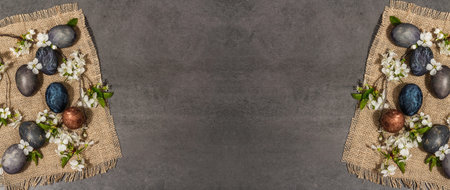 Easter eggs and blooming cherry on stone concrete background. Festive greeting card, traditional spring flowers. Modern hard light, dark shadow, flat lay, banner formatの写真素材