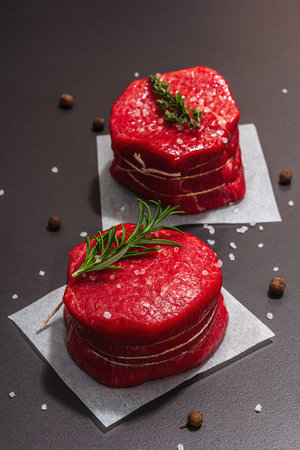 Raw Eye of round steak with spices and herbs on black stone concrete background. A trendy hard light, dark shadow, flat lay, close upの写真素材
