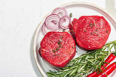 Raw Eye of round steak with spices and herbs on white background. Fresh meat for cooking healthy food. A trendy hard light, dark shadow, flat lay, top viewの写真素材