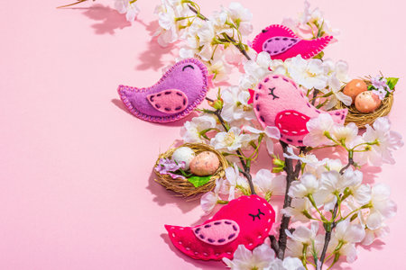 Gentle Easter composition with cherry flowers and handmade felt birds. Decorative eggs and nest, cute rabbits. Hard light, dark shadow, pink background, copy spaceの写真素材