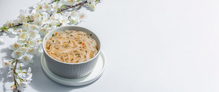 Korean noodles Ramen with broth. Hot dish, chopsticks, hard light, dark shadow. Gray background, cherry flowers, flat lay, banner formatの写真素材