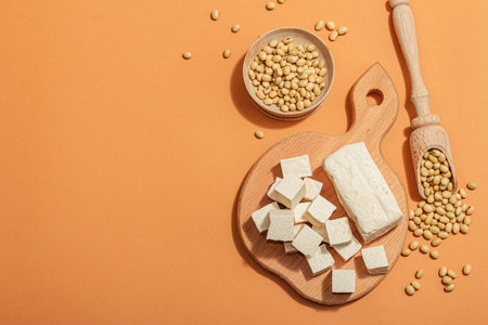 Fresh Tofu cheese with soybeans. Cube pieces, healthy ingredient for vegan lifestyle, modern stand, trendy hard light, dark shadow. Bright orange background, flat lay, top viewの写真素材