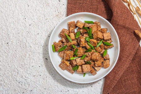 Fried teriyaki Tofu with scallions and sesame seeds. Healthy vegan meatless meal rich in protein and calcium. Trendy hard light, dark shadow, plaster background, top viewの写真素材