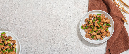 Fried teriyaki Tofu with scallions and sesame seeds. Healthy vegan meatless meal rich in protein and calcium. Trendy hard light, dark shadow, plaster background, banner formatの写真素材