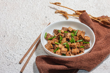 Fried teriyaki Tofu with scallions and sesame seeds. Healthy vegan meatless meal rich in protein and calcium. Trendy hard light, dark shadow, plaster background, copy spaceの写真素材