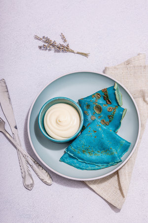Thin blue pancakes with creamy sauce. Healthy vegan non lactose and gluten free food, breakfast concept. Trendy hard light, dark shadow, light stone concrete background, top viewの写真素材