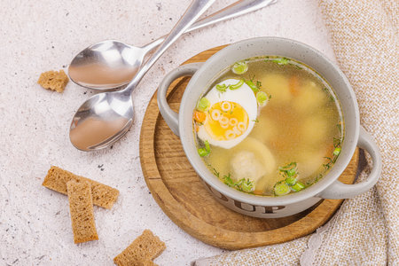 Meatball soup with boiled egg, ditalini pasta, vegetables and fresh herbs. Healthy chicken broth, traditional hot dish for dinner. Hard light, dark shadow, stone concrete background, top viewの写真素材