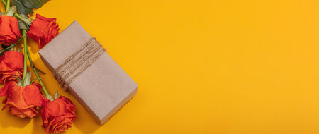 Zero waste gift concept. Bright roses, wrapped in craft paper surprise box for Anniversary, Mothers or Valentines Day. Happy birthday greeting card, orange background, banner formatの写真素材