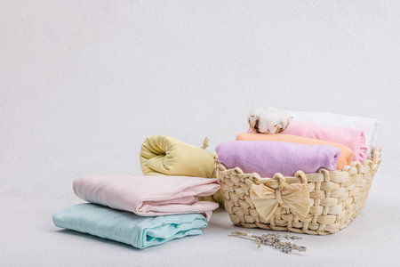 Vertical storage of clothing. Spring closet cleaning, eco friendly straw basket. Pastel colored baby T-shirts, folded after machine washing. Light stone concrete background, copy spaceの写真素材