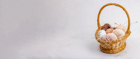 A set of pastel clew of thread for knitting in a basket. Handmade, hobby, crochet concept. Props and special craft tools on light stone concrete background, banner formatの写真素材