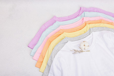 Vertical storage of clothing. Eco friendly spring closet cleaning. Pastel colored baby T-shirts, sale concept. Light stone concrete background, top viewの写真素材