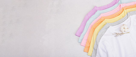 Vertical storage of clothing. Eco friendly spring closet cleaning. Pastel colored baby T-shirts, sale concept. Light stone concrete background, banner formatの写真素材