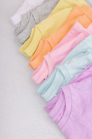 Vertical storage of clothing. Eco friendly spring closet cleaning. Pastel colored baby T-shirts, sale concept. Light stone concrete background, top viewの写真素材