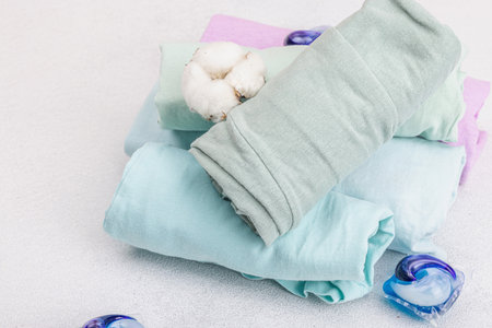 Eco friendly spring closet cleaning, capsules for machine washing. Pastel colored baby T-shirts, sale concept. Vertical storage of clothing. Light stone concrete background, copy spaceの写真素材