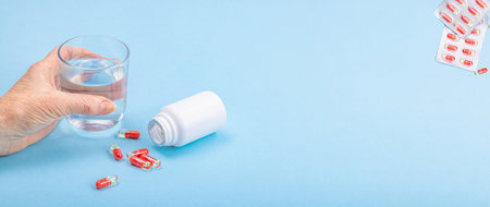 A woman takes medicine. Female hands hold capsules or pills. Treatment, taking vitamins, healthcare concept. Blue background, flat lay, banner formatの写真素材