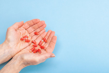 A woman takes medicine. Female hands hold capsules or pills. Treatment, taking vitamins, healthcare concept. Blue background, flat lay, top viewの写真素材