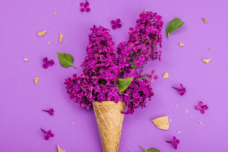 Violet lilac flowers in waffle ice cream cones on purple background. Flat lay, traditional spring concept, greeting card, hard light, dark shadow, top viewの写真素材