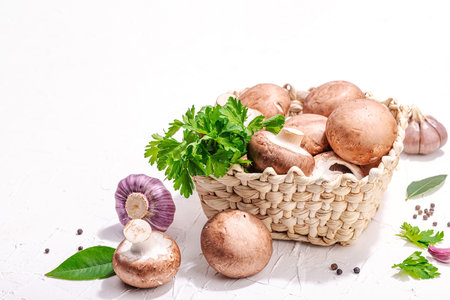 Raw brown royal champignons in the basket. Cooking vegan food concept. Garlic, greens, spices, hard light, dark shadow. Edible mushrooms, a modern trend, white background, copy spaceの写真素材