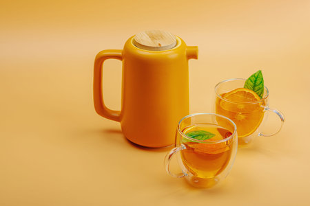 Orange tea in ceramic tea pot with ripe fruits. Refreshment seasonal drink, conceptual background with green citrus leaves. Modern style, selective focus, copy spaceの写真素材
