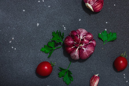 Culinary background with fresh vegetables and herbs. Tomatoes cherry, garlic, sea salt, and parsley. Flat lay, hard light, dark shadow, black stone concrete backgroundの写真素材