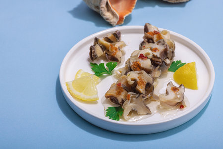 Pickled rapan meat with oil, spices and greens. Healthy seafood rich of omega. Marine decorative prop, hard light, dark shadow, blue background, copy spaceの写真素材