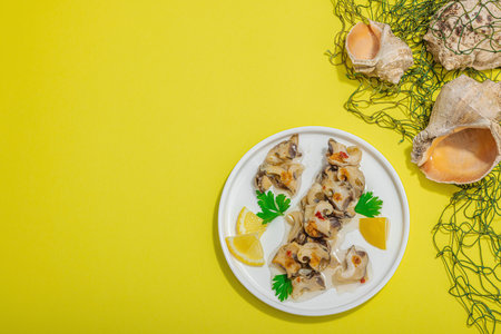 Pickled rapan meat with oil, spices and greens. Healthy seafood rich of omega. Marine decorative prop, hard light, dark shadow, yellow background, top viewの写真素材