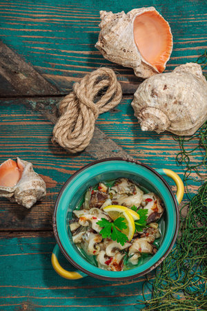 Rapana clam meat with oil, spices and greens. Healthy seafood rich of omega. Marine decor, hard light, dark shadow, old wooden boards, top viewの写真素材