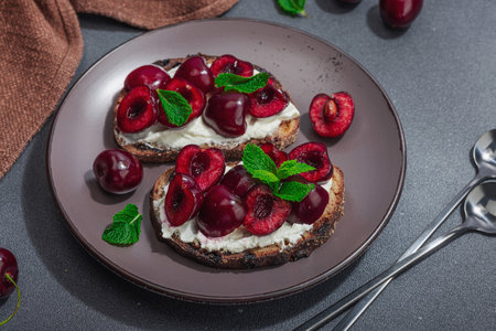 Fresh bread sandwiches with sweet cherry, cream cheese and mint leaves. Good morning breakfast concept. Hard light, dark shadow, black stone concrete background, close upの写真素材