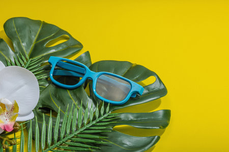 Summer vacation concept. Sunglass, marine decor, palm and monstera leaves, orchid flower. Bright yellow background, hard light, dark shadow, flat lay, copy spaceの写真素材