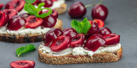 Fresh bread sandwiches with sweet cherry, cream cheese and mint leaves. Good morning breakfast concept. Hard light, dark shadow, black stone concrete background, banner formatの写真素材