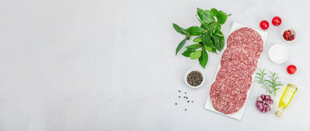 Raw burger patties. Fresh meat cutlets, spices, vegetables and herbs. Homemade American classic, traditional food for picnic, party or Independence Day. Light stone concrete background, banner formatの写真素材