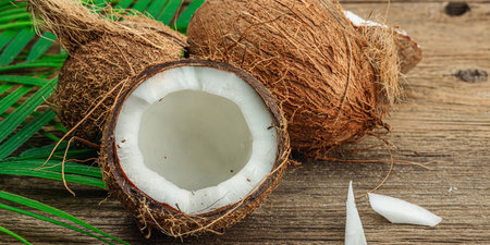 Summer tropical background with coconuts and palm leaves. Traditional decor, textured fruit, voyage concept. Old wooden boards background, flat lay, banner formatの写真素材