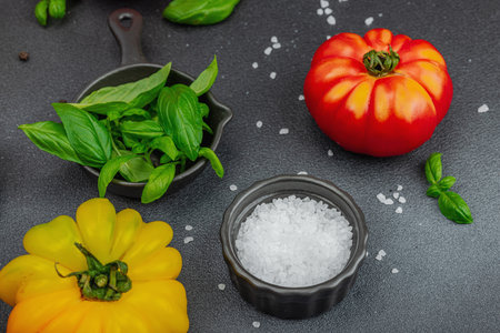 Colorful Heirloom tomato harvest. Ripe ribbed vegetables with fresh basil leaves. Juicy ingredient for summer salad and spices. Black stone background, flat lay, close upの写真素材