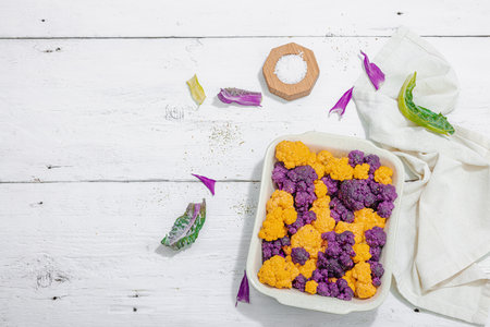 Cauliflower, yellow and purple, ready to bake. Healthy food, spices, olive oil. Hard light, dark shadow, white wooden background, top viewの写真素材