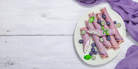 Thin purple pancakes with cream and blueberries. Healthy vegan non lactose and gluten free food, breakfast concept. Trendy hard light, dark shadow, white wooden background, banner formatの写真素材