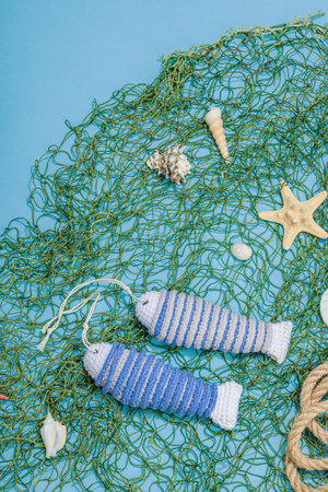 Handmade marine concept. Crocheted sardine fishes, nautical style. Fishing net, traditional sea decor. Hard light, dark shadow, trendy blue background, top viewの写真素材