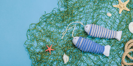 Handmade marine concept. Crocheted sardine fishes, nautical style. Fishing net, traditional sea decor. Hard light, dark shadow, trendy blue background, banner formatの写真素材