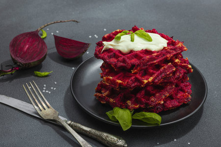 Homemade beetroot Belgian waffles with sauce. Gluten free vegan food with vegetables. Trendy hard light, dark shadow, black stone concrete background, close upの写真素材