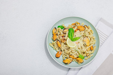 Plant based pasta with mussels, pesto and parmesan cheese. Ready to eat healthy food, served portion on stone table. Hard light, dark shadow, flat lay, top viewの写真素材