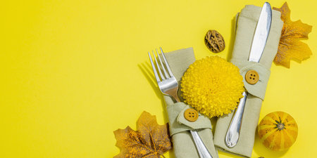 Autumn table setting. Thanksgiving cutlery, traditional fall decor, flat lay. Festive cozy mood, pumpkin, leaves, bright yellow background, banner formatの写真素材