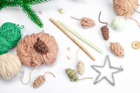 Creative handmade winter flat lay. Cozy crocheted pine cones, traditional decor, tools, craft mood concept. White background, evergreen Christmas tree branch, top viewの写真素材